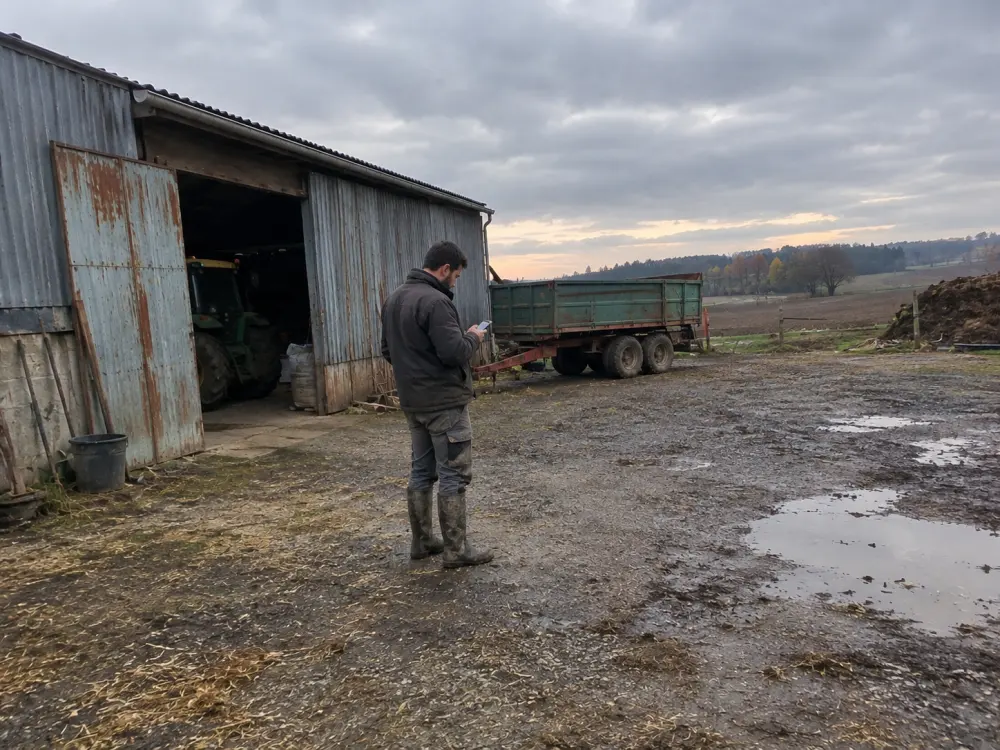 Un salarié agricole note sa journée sur son téléphone dans la cour de la ferme