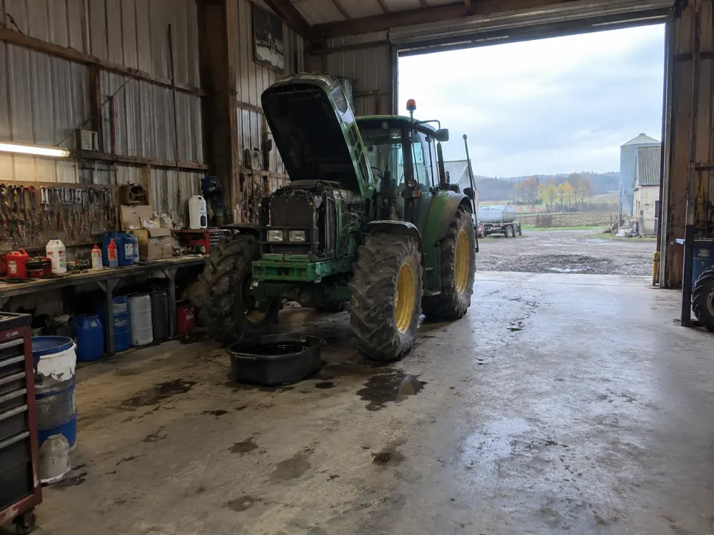 Un tracteur capot ouvert dans l’atelier de la ferme, pendant une vidange
